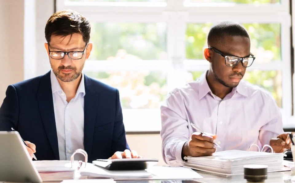 Two men in an office environment working at laptops on the same desk